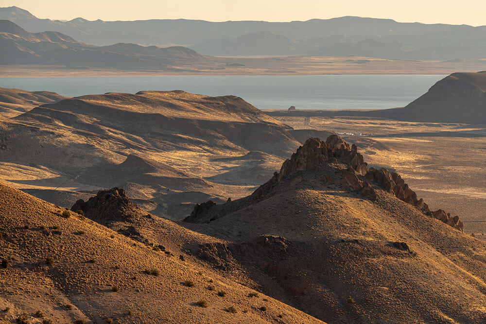 Desert lake surrounded by mountains, taken from above, golden hues in the sky and ground.