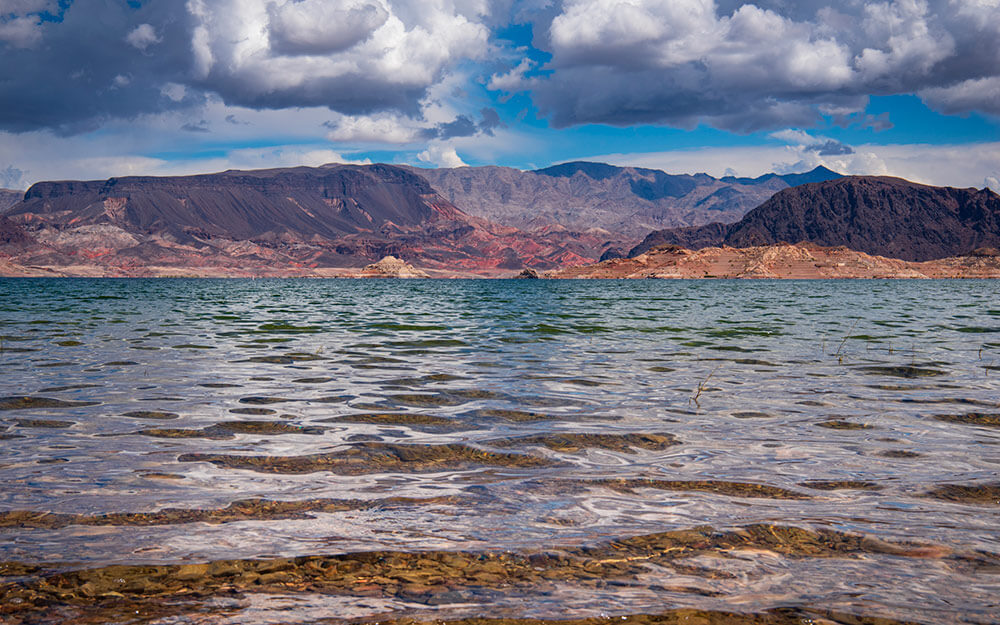 Desert lake with mountains in the background and cloudy blue sky.
