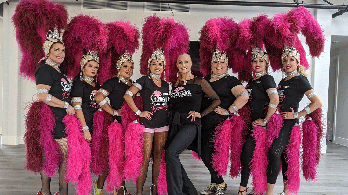A group of women pose for a photo dressed in showgirl attire.