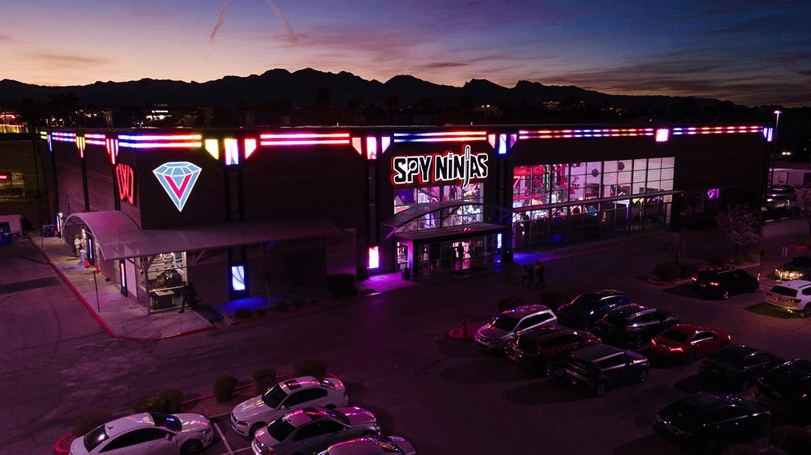 Spy Ninjas HQ building lit up with neon lights during dusk.