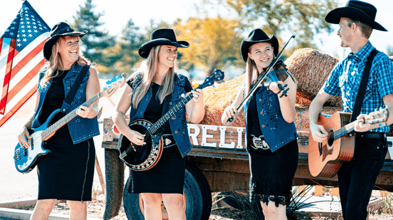 The Firelight Barn Dinner Theater bandmates pose for a photo outside while playing and are dressed in black and denim.