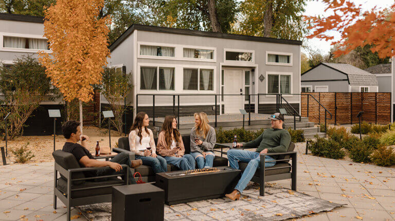 A group of friends hangs outside in front of a fire pit located near one of River West Resort's Pearl Gem Cottage.