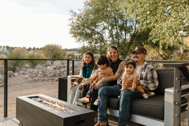 A family of five sit outside on a couch in front of a fire pit at River West Resort in Reno.