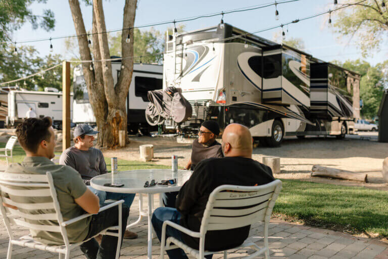 A group of men sit at an outdoor patio laughing, all outside of RVs at River West Resort in Reno.