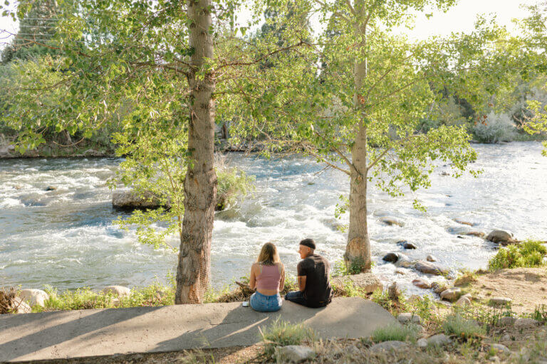 A man and woman sit on a concrete wall overlooking the Truckee River in Reno.