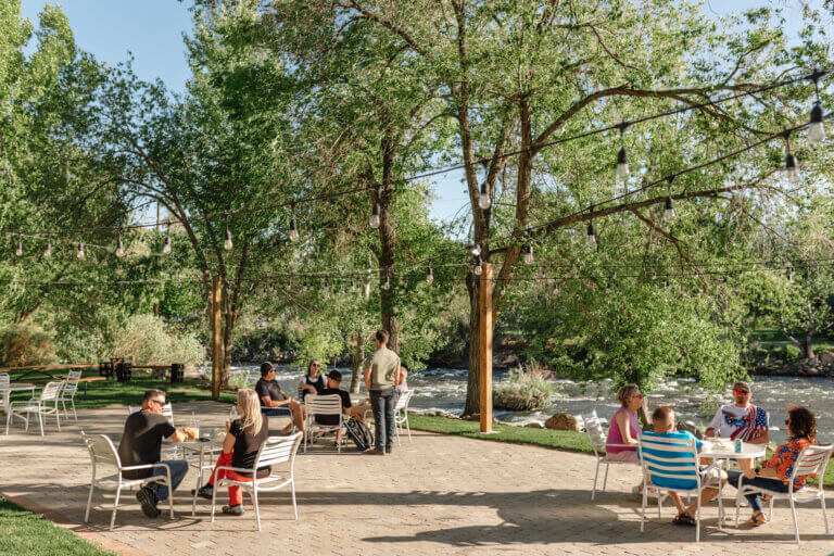 People sit at various tables on a patio located next to the Truckee River in Reno.