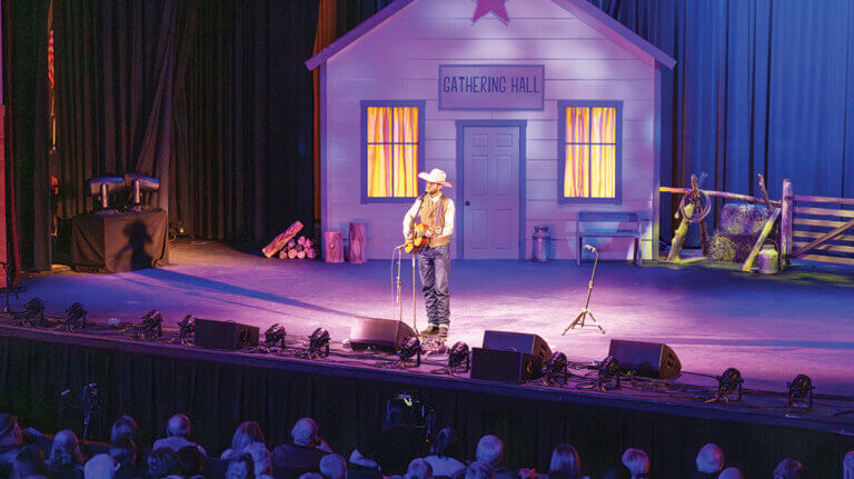 lone performer with a guitar on stage at cowboy poetry in elko